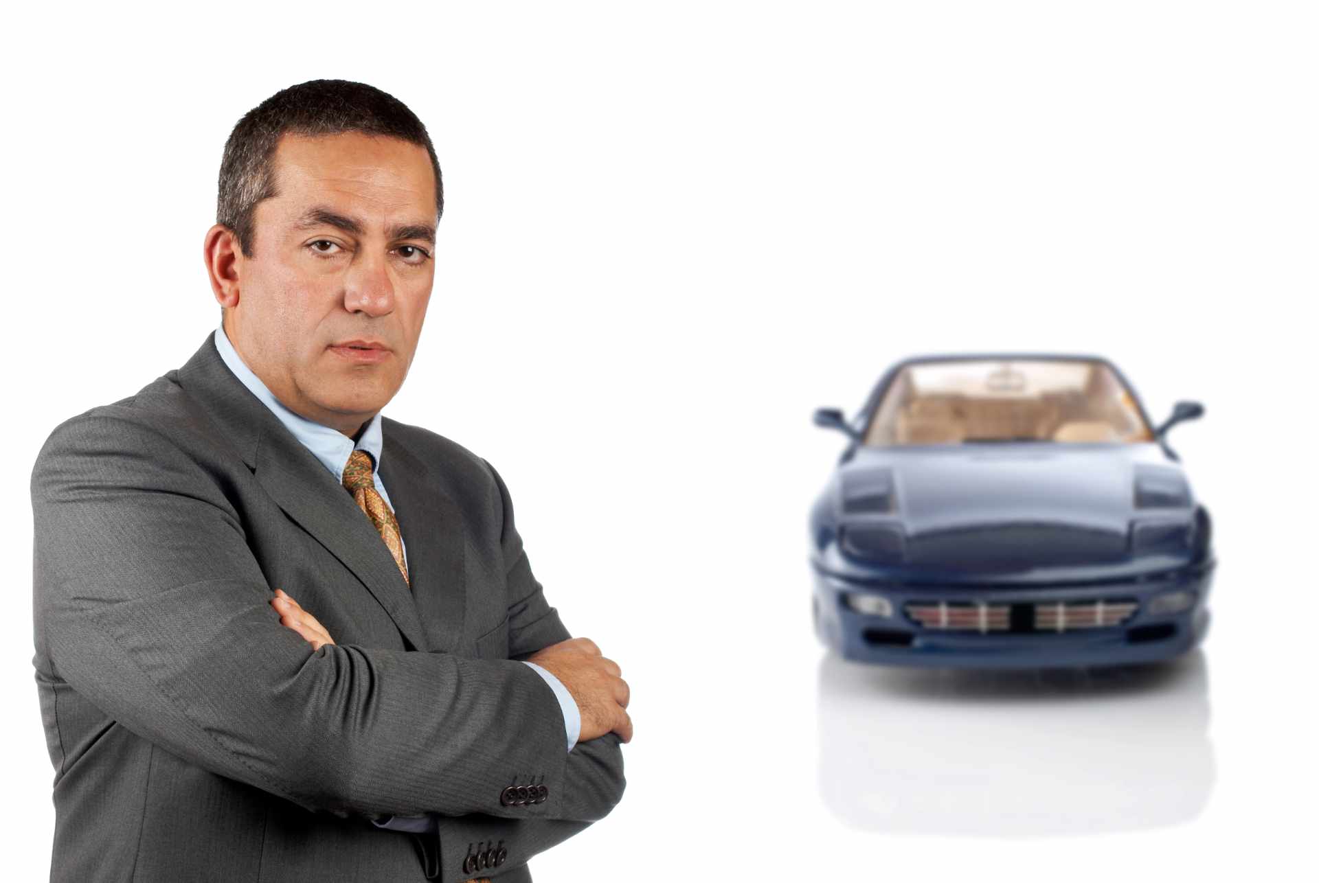 Business professional in gray suit standing confidently with a blue sports car, symbolizing trust and success in auto dealer bond cost discussions